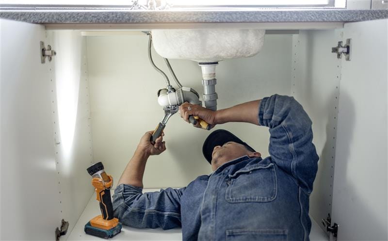 Plumber repairing pipes beneath a bathroom sink in Manteca